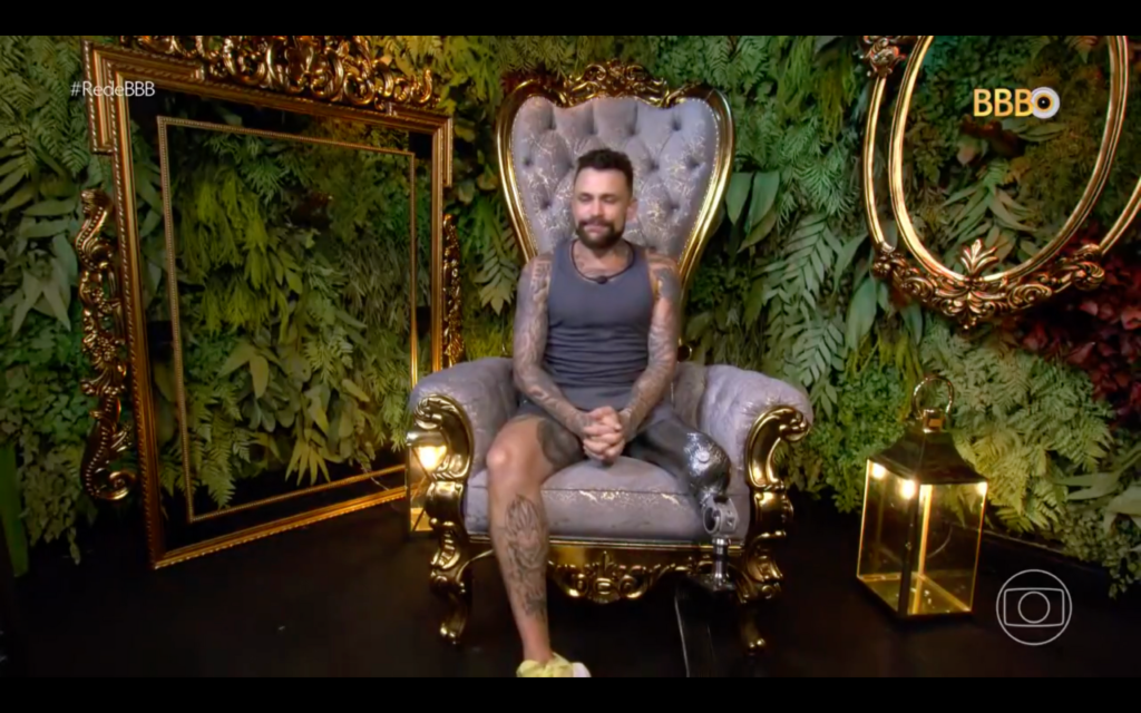 #descriçãodaimagem #pratodosverem print da tela do programa BBB. O participante Vinicius está no confessionário. Ele é amputado e usa uma prótese de perna esquerda.