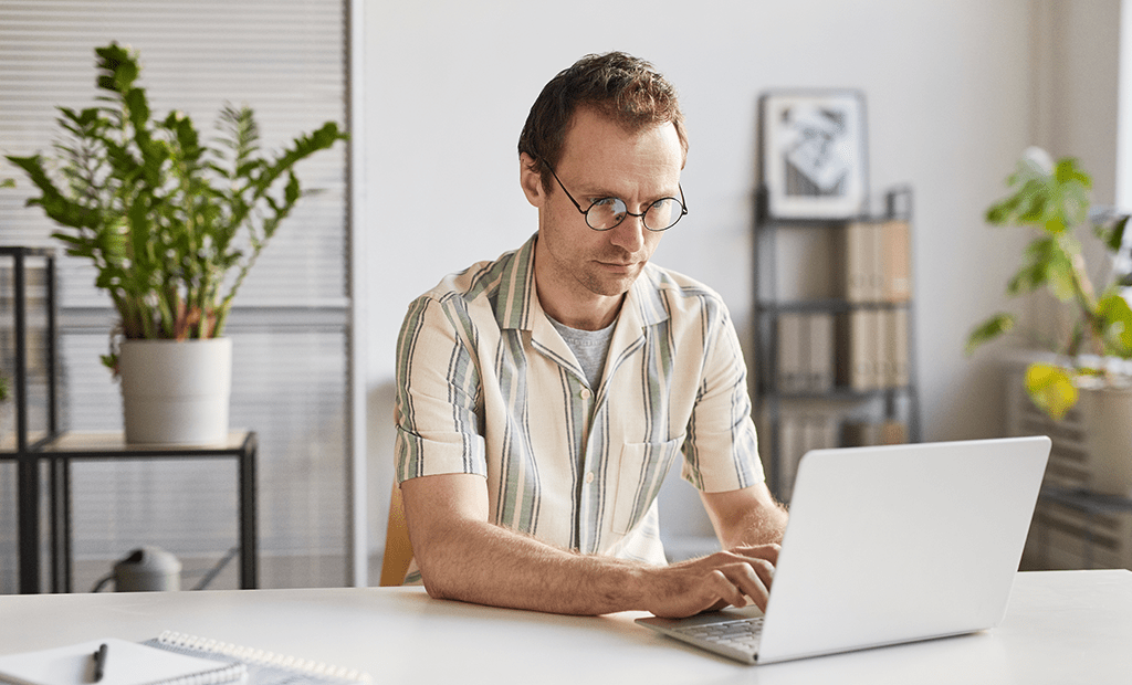 #descriçãodaimagem #pratodosverem foto de um homem branco e de óculos com cabelos ruivos, mexendo no notebook em uma sala.