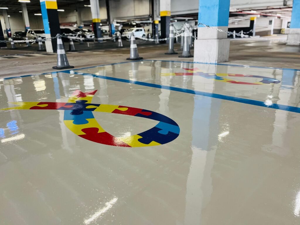 #descriçãodaimagem #pratodosverem foto das vagas reservadas para autistas, com o desenho do laço colorido formado por peças de um quebra-cabeça, no estacionamento do shopping.
