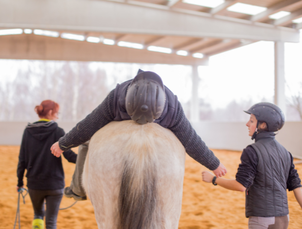 #descriçãodaimagem #pratodosverem foto de uma pessoa durante o atendimento de equoterapia. A pessoa está deitada sobre um cavalo branco e duas profissionais da equipe de equoterapia estão ao lado do cavalo.