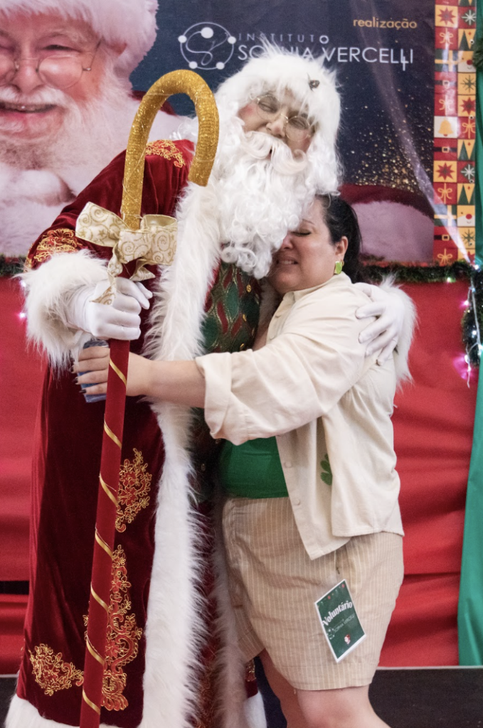 #descriçãodaimagem #pratodosverem foto de uma mulher abraçando o Papai Noel.